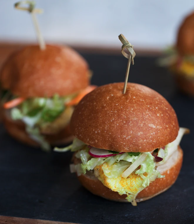 Close-up image of gourmet sliders with decorative bamboo skewers on a black marble surface.