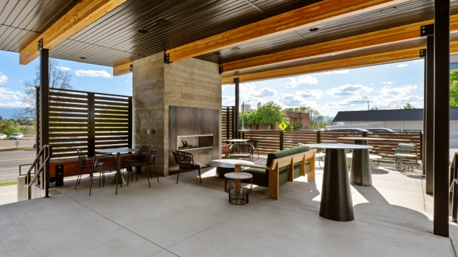 Modern outdoor patio with mixed seating, wood beams, and a concrete fireplace under a covered roof structure