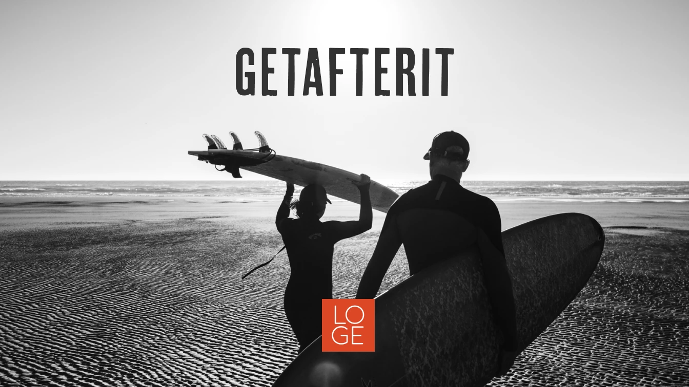 Two surfers walking towards the ocean with surfboards under their arms. The text "GETAFTERIT" is prominently displayed at the top center of the image. Below the text, there is a small red square with the white "LOGE" logo. The image is in black and white, capturing the serene beach and horizon in the background.