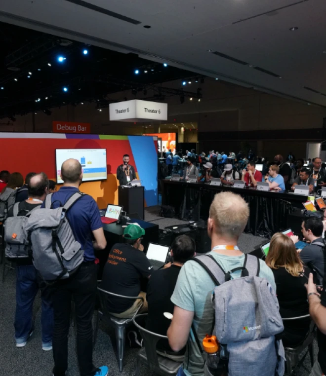 A busy scene at a Microsoft Learn event with attendees gathered around a speaker at the front, delivering a presentation.