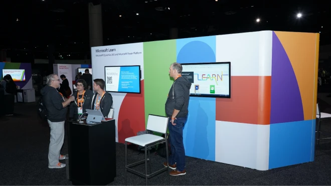 Four people interacting at a Microsoft Learn Event booth that highlights the Microsoft Dynamics 365 and Microsoft Power Platform.