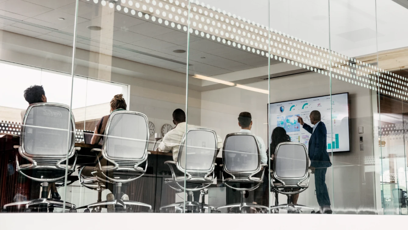 A group of professionals in a modern conference room, viewed through a glass wall, attending a presentation.