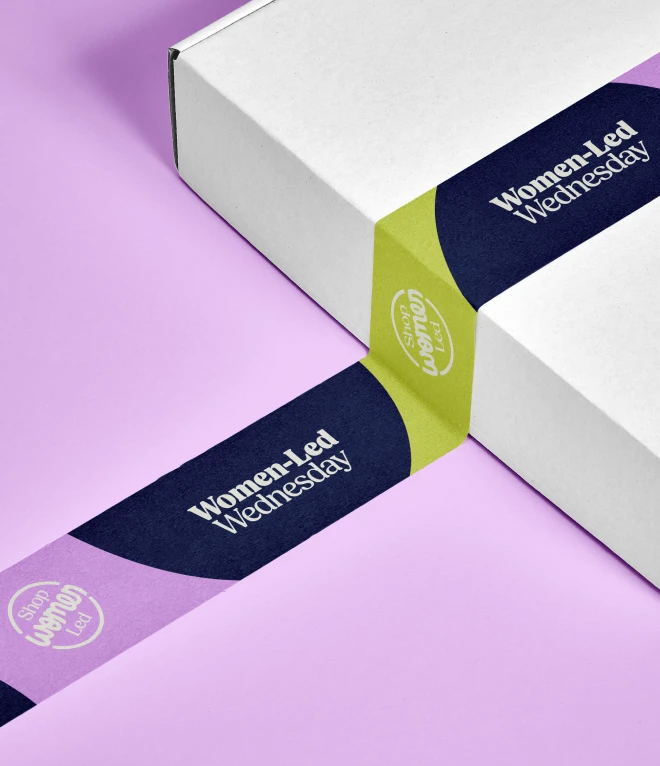 A white cardboard box sealed with decorative tape featuring the "Women-Led Wednesday" branding against a lavender surface.